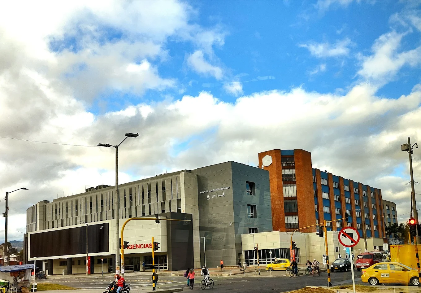 Vue de la rue d'un bâtiment hospitalier avec un ciel bleu et des nuages.