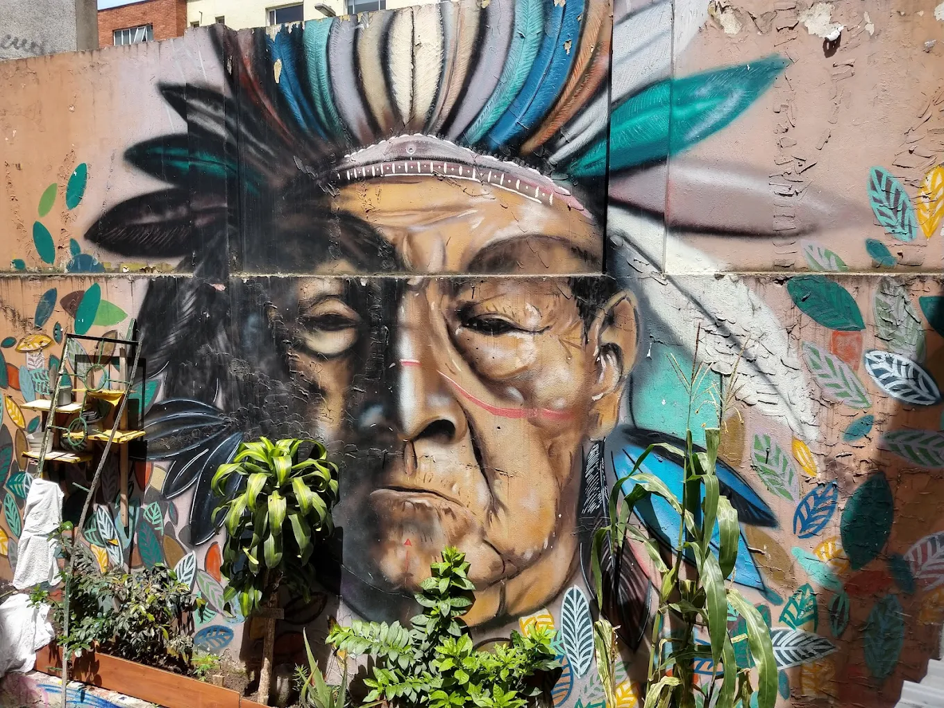 une peinture murale extérieure représentant le visage d'une personne avec une coiffe en plumes