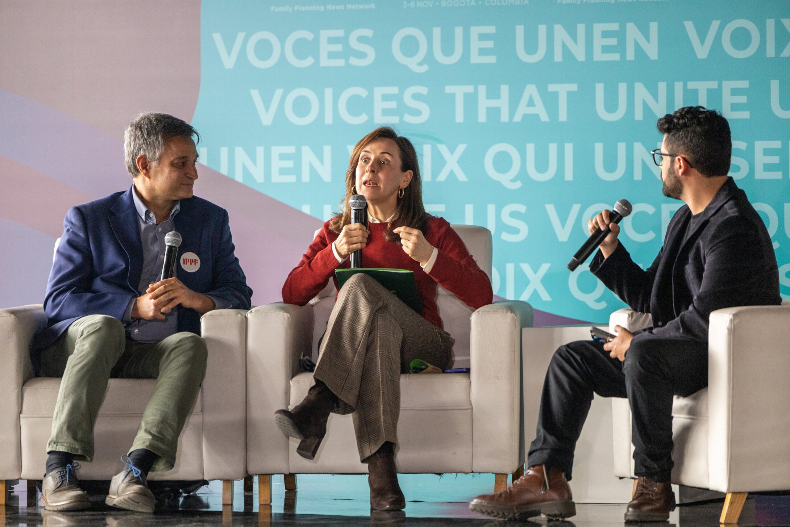 three people holding microphones and sitting in white chairs on a stage