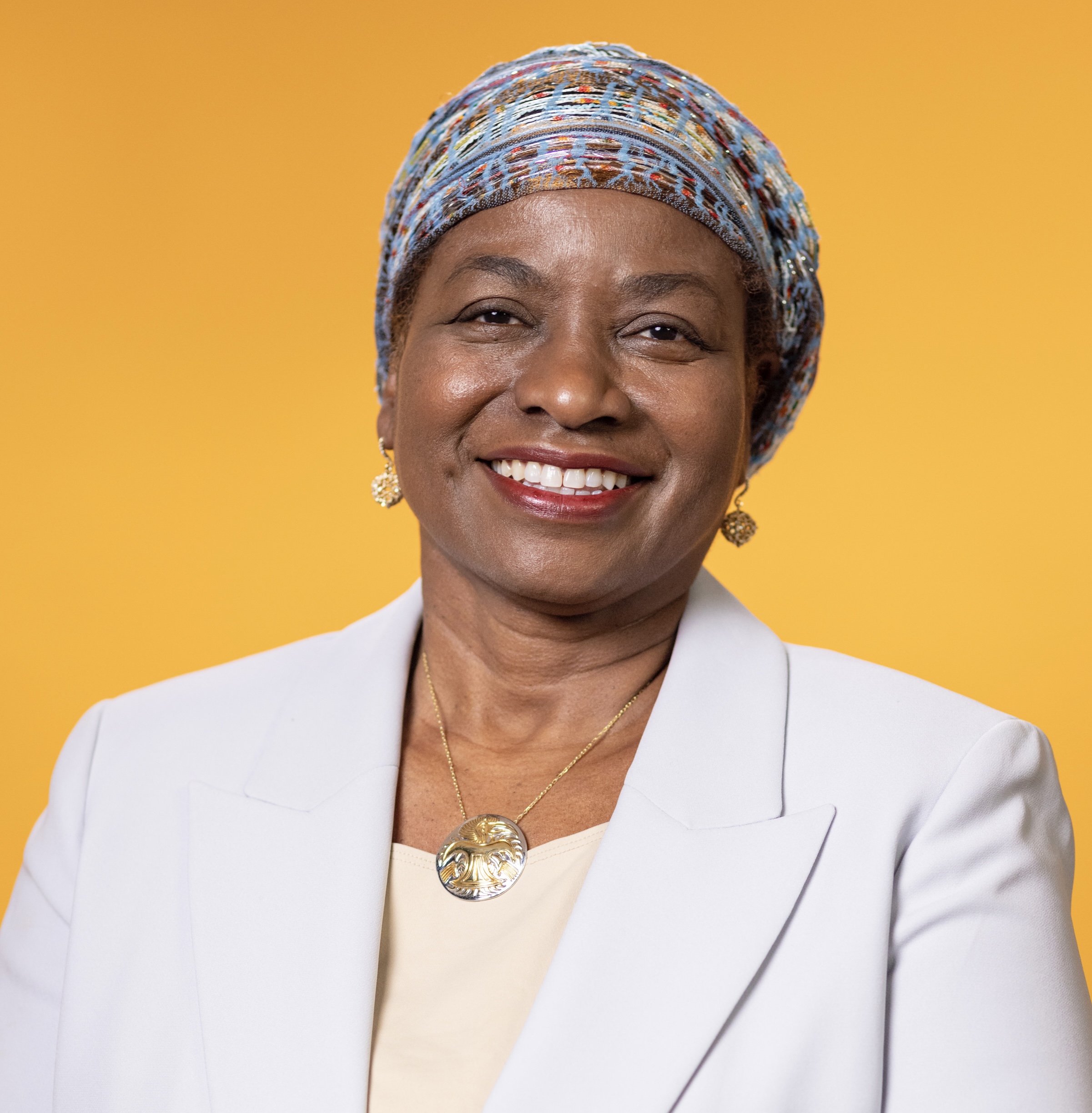 A headshot of a woman with a yellow background and white blazer